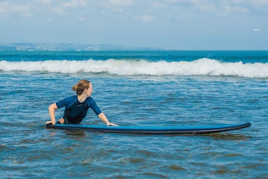Beginner surfer sitting on a surfboard in shallow water, preparing to paddle out.