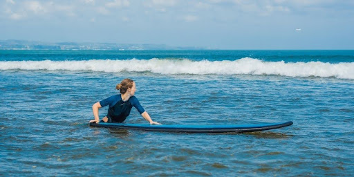 Beginner surfer sitting on a surfboard in shallow water, preparing to paddle out.