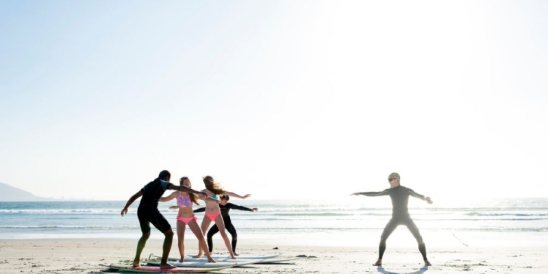 A group learning to surf, practicing stances on the beach with an instructor