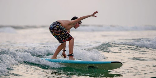 Beginner surfer mid-pop-up on a wave, maintaining balance on a longboard. 